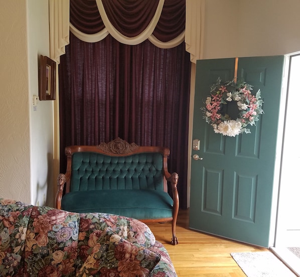 Front of living room with green velvet antique sofa and front door open