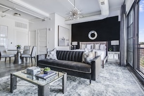 Living area with large bed, sofa, coffee table, and a table with chairs in the corner.