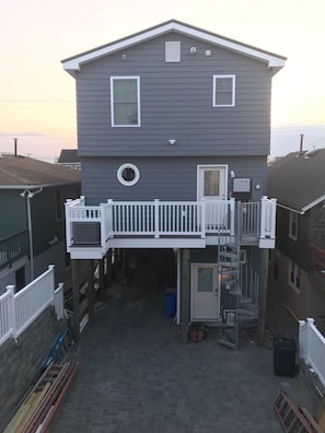 Beach side of house. Back deck with stairs leading down. Grill and table.