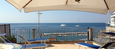 Terrazza vista mare con tavolo in ceramica, sedie lettini e ombrellone