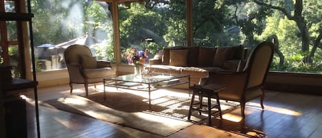Living room walls of glass with views to patio surrounded by large oaks