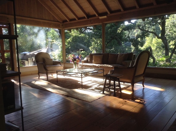 Living room walls of glass with views to patio surrounded by large oaks