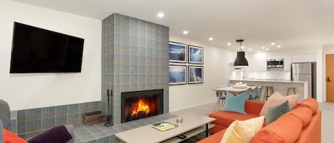 Lounge features a stone-surround presto log fireplace, TV, and sliding door access to the deck