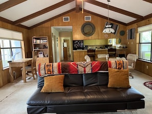 Living room with vaulted ceiling, futon sofa, dinning table, desk & chair. 