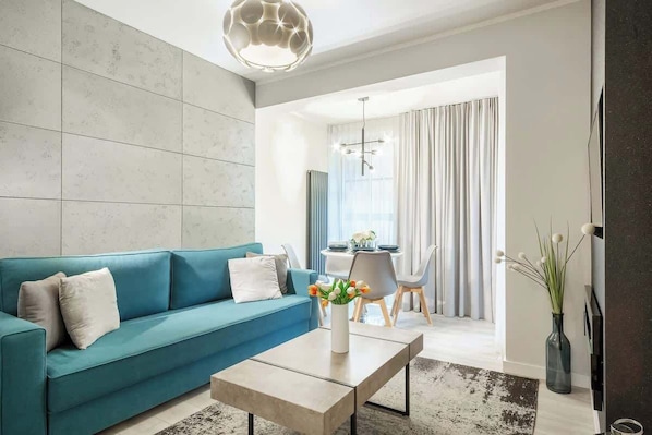 Atmopsheric and air conditioned living room with intensive blue double sofa bed, coffee table, and dining table with chairs.