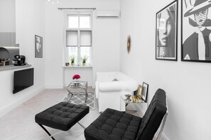 Elegant and stylish living area with a white sofa, a coffee table, an armchair, and a kitchenette.