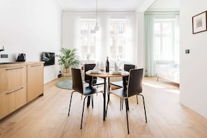Modern and stylish living area with dining table, chairs for four people, functioal cabinet, and television.