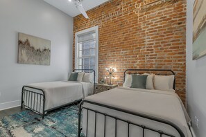 Spacious guest bedroom with two full-size beds and a designer built-in closet. Features a nightstand, lamp, hangers, luggage rack, alarm clock, white noise machine, and a 50'' Samsung Smart 4K TV with streaming and DIRECTV Entertainment.