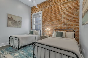 Spacious guest bedroom with two full-size beds and a designer built-in closet. Features a nightstand, lamp, hangers, luggage rack, alarm clock, white noise machine, and a 50'' Samsung Smart 4K TV with streaming and DIRECTV Entertainment.