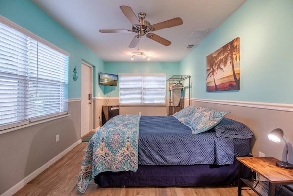 room with queen size bed, mini refrigerator, tv, closet, clothes hangers, ironing board, ceiling fan