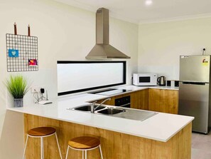 Modern kitchen with Ninja blender, toaster, kettle, fridge/freezer, microwave, oven and cooktop plus a good selection of cooking utensils