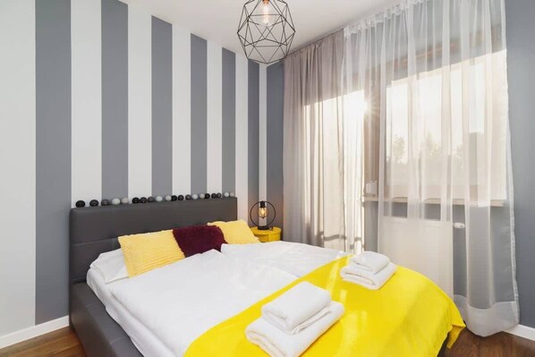 A bedroom with gray and white striped wallpaper, a double bed featuring yellow and white bedding, and a modern, cozy ambiance.
