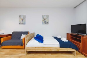 A combined bedroom and sitting area with a wooden bed, a small couch, and natural light from large windows.