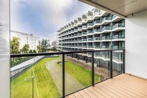 A balcony overlooking a lush green outdoor space with modern architecture visible in the background.