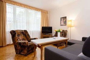 A vintage-style living room with a double sofa bed, TV and two retro-style armchairs.