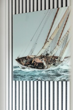 : A painting of a sailboat on the wall, framed against striped wallpaper.