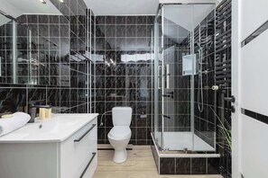 The same black-tiled bathroom, showing a close-up of the shower and sink area.