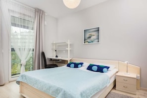 A cozy bedroom with a double bed, blue bedding, and a simple yet functional storage shelf and wardrobe. The room is well-lit and relaxing.