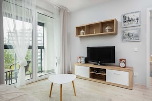 A view of the living room that includes a media console, television, and access to a spacious balcony with greenery visible outside.