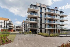 A view of the apartment building showcasing its multi-story structure, balconies, and well-maintained outdoor pathway. The facade is modern and sleek.
