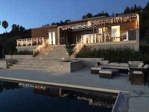 Back of house with pool, hot tub and seating area with fireplace.
