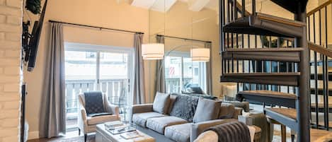 Open living room with vaulted ceiling, gas fireplace, and balcony access 