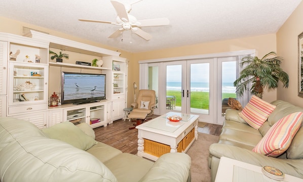 Living room with a smart TV, sofas, ceiling fan, and sliders to the oceanfront patio