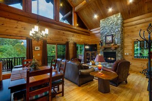 Large living room has satellite tv, gas log fireplace, comfortable seating and vaulted ceiling framed by natural log beams.. 