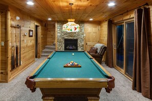 The lower level game room has a regulation size pool table, gas log fireplace, bathroom, TV and sofa 
