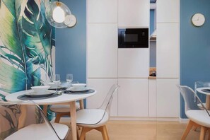 A cozy dining area with a small table and chairs, decorated with tropical-themed wallpaper featuring green leaves.