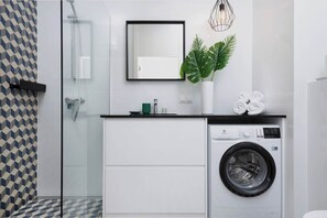 A compact bathroom featuring a washing machine, sink, and minimalist decor with white and gray tones.