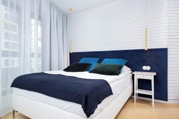 A modern bedroom with navy and white bedding on a double bed, complemented by light wooden furniture and a bright atmosphere.