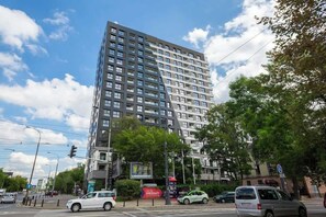 A high-rise apartment building with a modern facade, surrounded by greenery and parked cars.
