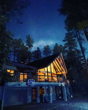 The cabin glows at night under the stars and ponderosa pines.
