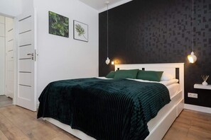 A stylish bedroom with a queen-size bed, dark feature wall, green bedspread, and white furniture, providing a contemporary look.