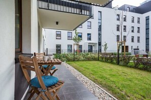 A view of an outdoor garden area with a small patio space, including chairs for relaxation in front of a residential building.
