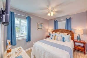 Queen Bed in the Bedroom, with a window and view of the outdoor pool. There is a closet with hangers and shelves and a dresser. A small smart tv is located in the bedroom.