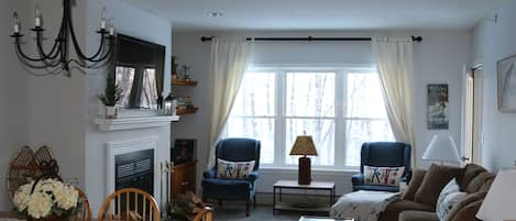 Large comfy living room with big flatscreen TV over wood burning fireplace