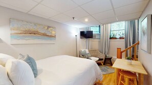 Bed, wall art, lounge chair, mounted TV, table with stools, window