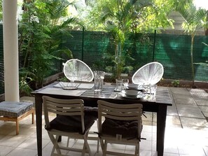 La terrasse couverte, dotée d'un coin repas, qui s'ouvre sur le petit jardin. 