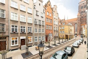A charming view of a narrow street lined with colorful, historic buildings, typical of European architecture, with cars parked along the cobblestone road.