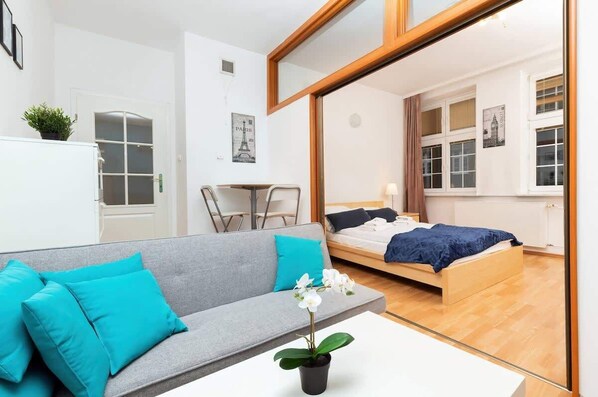 A cozy, modern living room with a vibrant turquoise couch and wooden beams on the ceiling, featuring a small coffee table and a TV, creating a bright and welcoming atmosphere.