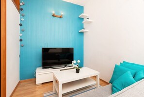 The comfortable living room, with a vibrant turquoise sofa, is furnished with a small coffee table and TV, creating a bright and welcoming atmosphere.