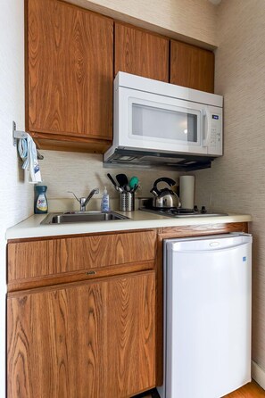 A compact kitchenette featuring a mini-fridge, two burner stove, and microwave for your convenience.