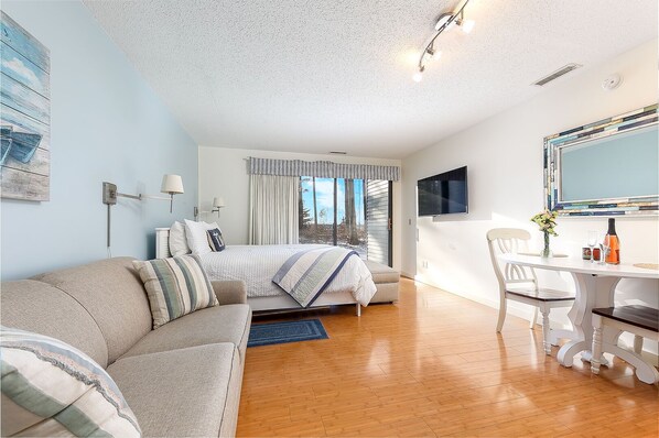 The unit features a queen-size bed, a queen-size pull-out sleeper sofa, a balcony, a dining table for two, a flat-screen TV, and a scenic garden view.