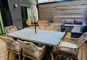 Private Rooftop Terrace: Luxurious and brand new, perfect for dining, lounging, and relaxing with big groups. Features multiple seating areas, dining sectional chairs, a BBQ, and festive night lights around the fence.