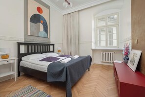 A bright bedroom with a double bed, red ottoman, large windows, and minimalistic decor