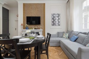 A comfortable living room with a dining table and chairs, couch, and a TV mounted on the wall.