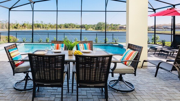 Relax by the pool with a lake view! Cozy seating, colorful pillows, and a fresh outdoor dining setup await you.