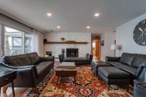 Large Living room with leather couches, wood fireplace, and large doors overlooking the lake